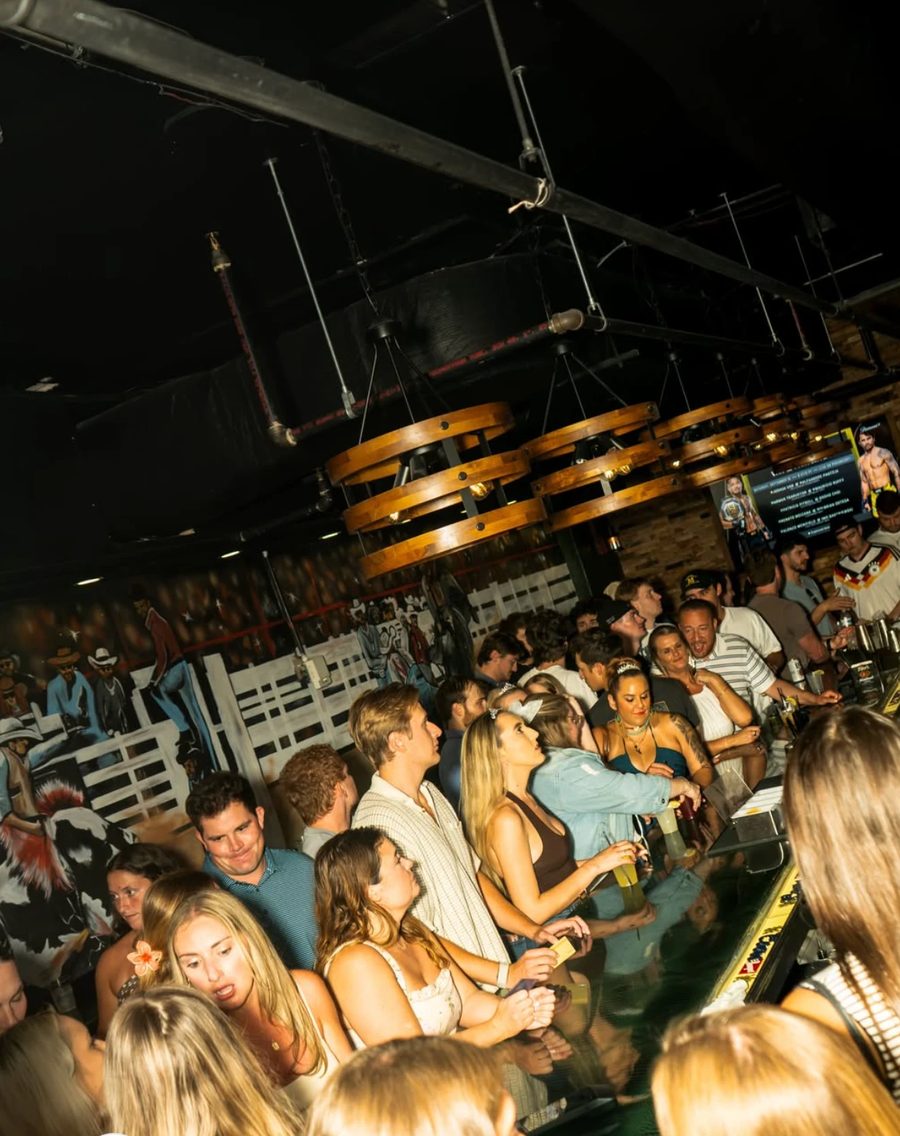 A crowded bar at BOE in Clarendon on a weekend night, under wagon-wheel lights with a western mural behind