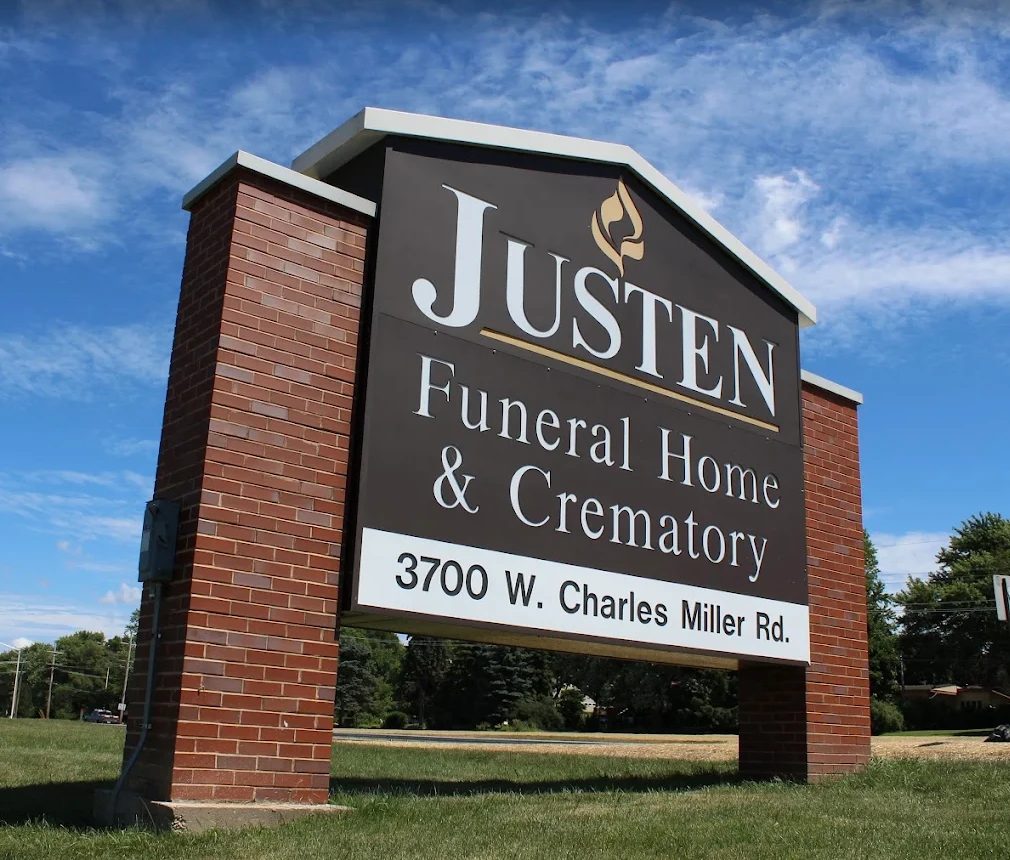 The brick and wood sign for Justen Funeral Home and Crematory at 3700 W Charles Miller Rd, McHenry, Illinois, under a blue sky