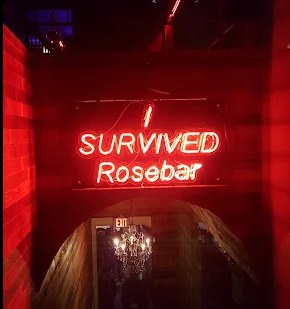 A red neon sign reading I Survived Rosebar above a brick archway